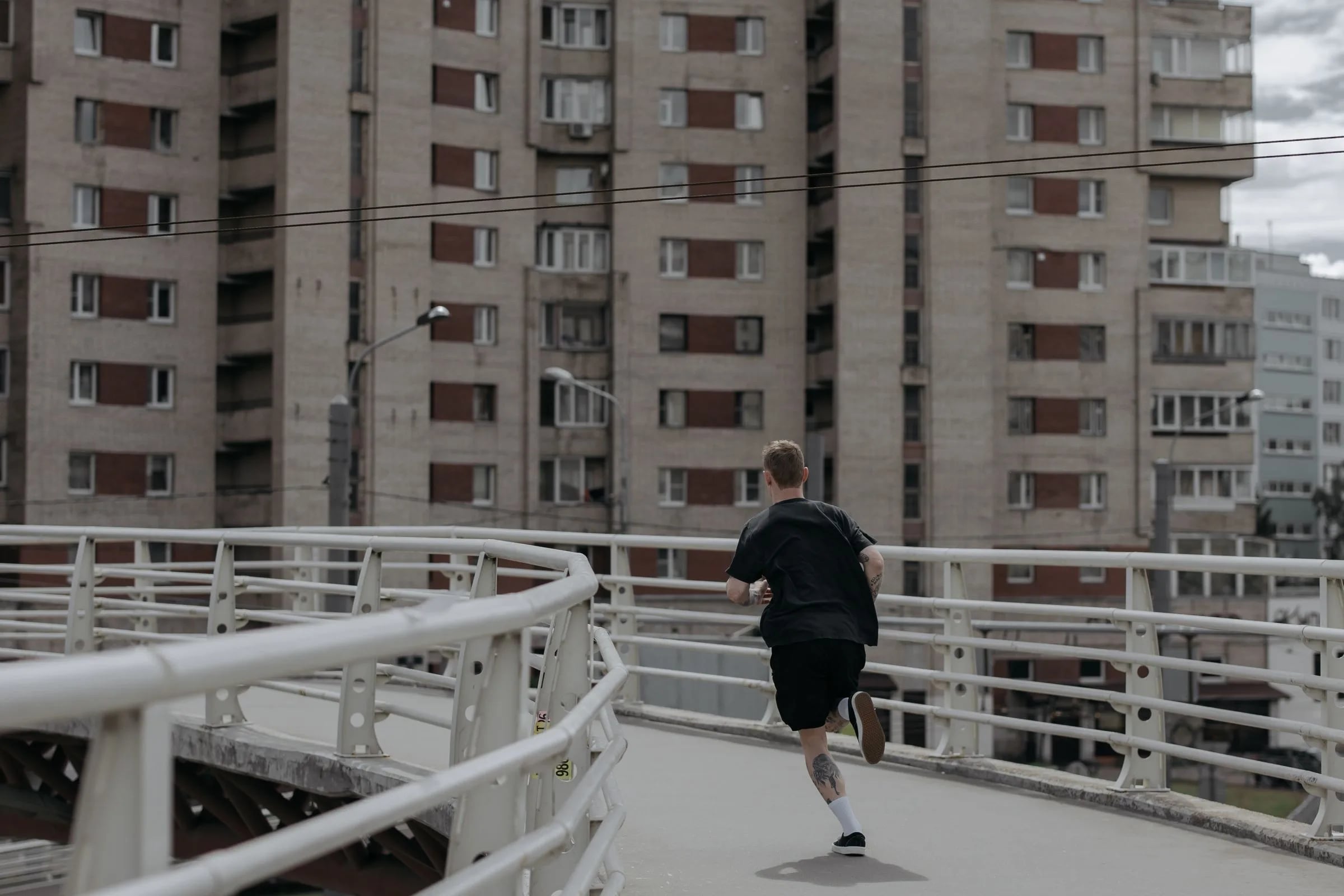 A runner crossing a white-railed footbridge in flat overcast light